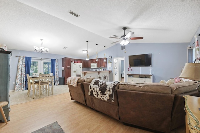 living room featuring lofted ceiling, ceiling fan with notable chandelier, light wood-type flooring, and a textured ceiling