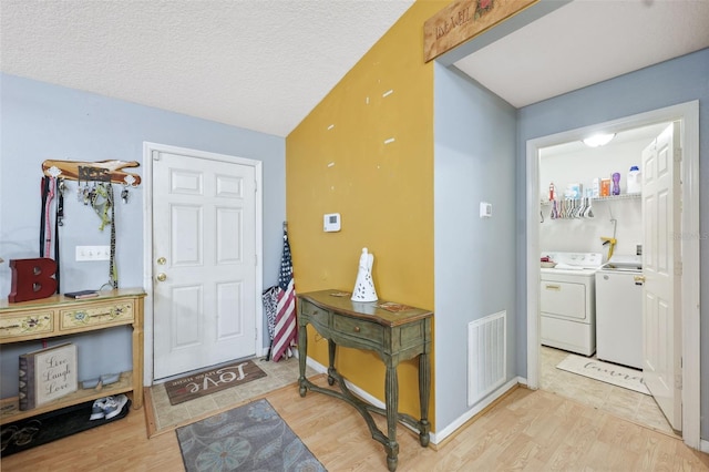 entryway featuring separate washer and dryer, light hardwood / wood-style flooring, and a textured ceiling