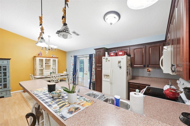 kitchen featuring a notable chandelier, hanging light fixtures, white appliances, light hardwood / wood-style floors, and a textured ceiling