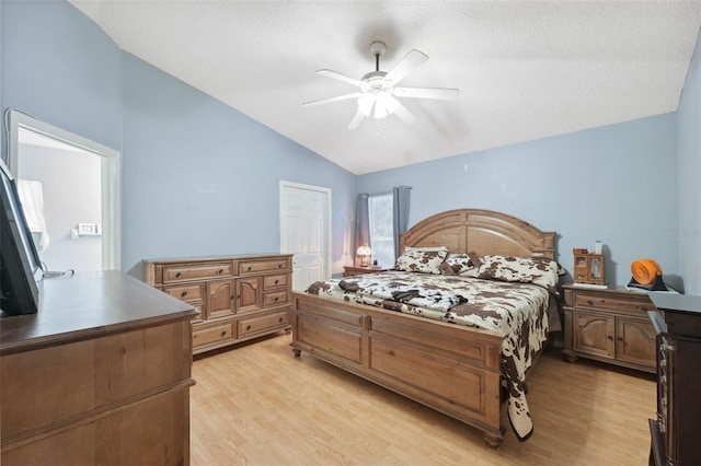 bedroom with vaulted ceiling, a textured ceiling, ceiling fan, and light wood-type flooring