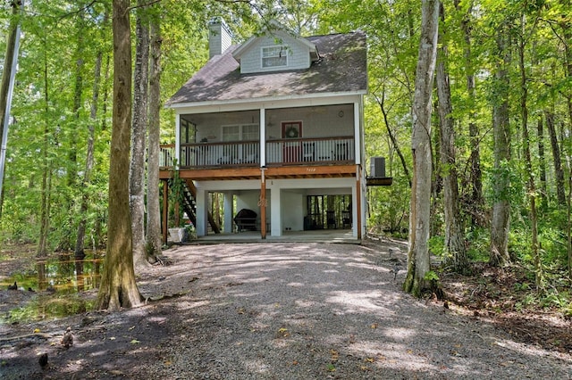 view of front of property featuring a chimney, stairway, a carport, driveway, and a forest view