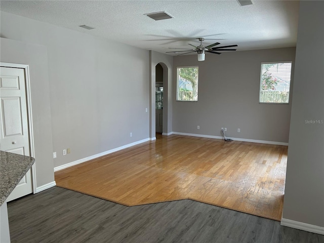 empty room with a textured ceiling, a healthy amount of sunlight, ceiling fan, and dark hardwood / wood-style floors