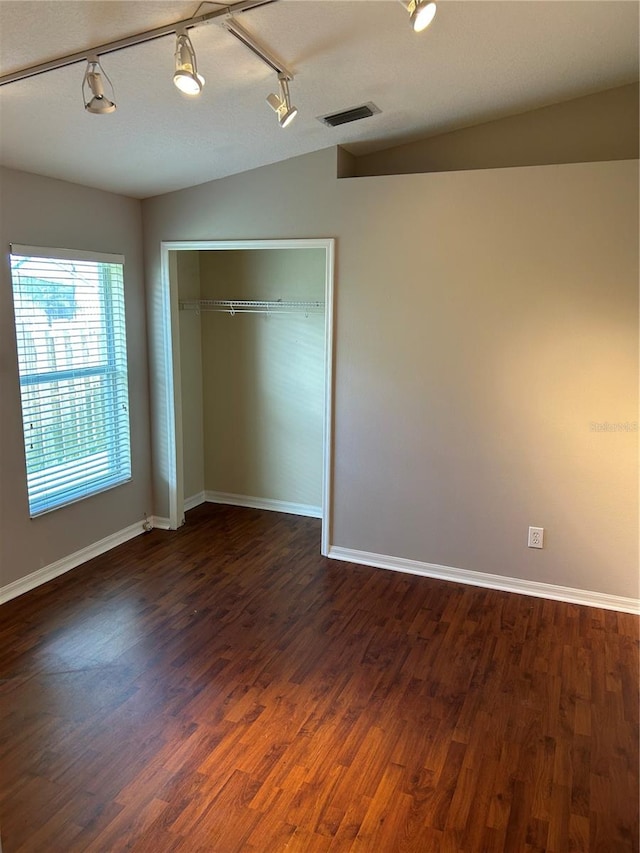 unfurnished bedroom with a closet, hardwood / wood-style flooring, vaulted ceiling, and rail lighting