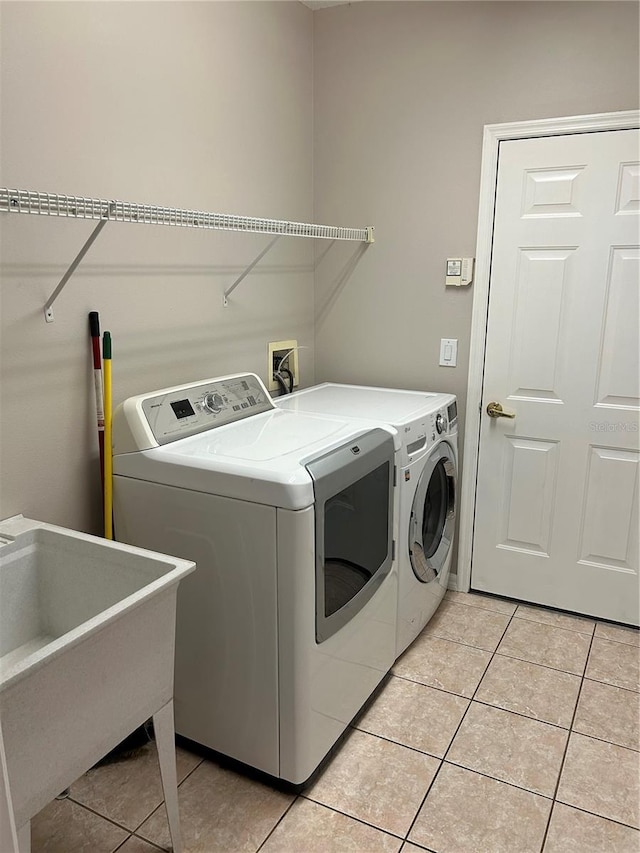 clothes washing area featuring washer and clothes dryer, sink, and light tile patterned floors