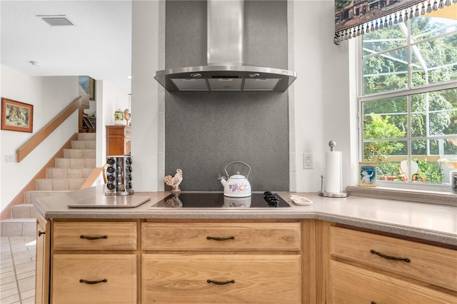 kitchen featuring black electric stovetop, wall chimney exhaust hood, and light brown cabinetry