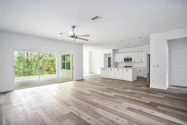 unfurnished living room featuring sink, ceiling fan, and light wood-type flooring