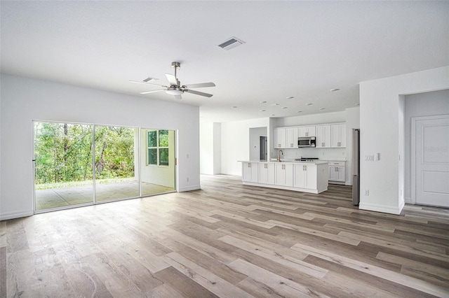 unfurnished living room with ceiling fan, sink, and light wood-type flooring