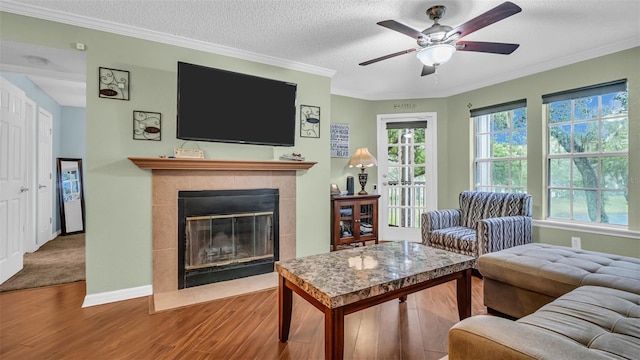 living room with wood-type flooring, ceiling fan, plenty of natural light, and a tiled fireplace