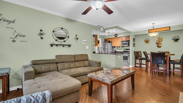 living room with ceiling fan, crown molding, hardwood / wood-style floors, and a textured ceiling