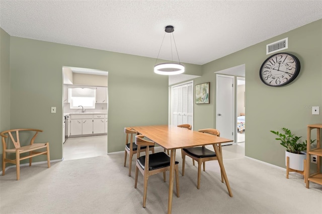 dining room featuring sink, light carpet, and a textured ceiling