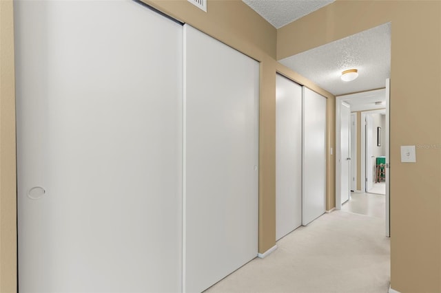 hall featuring light carpet and a textured ceiling