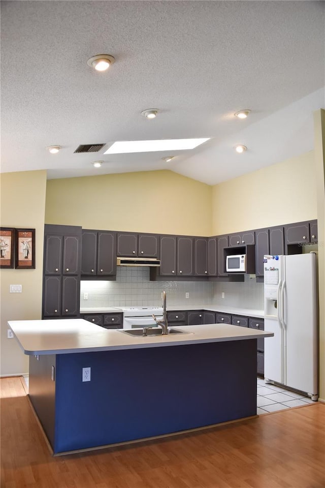 kitchen featuring sink, white appliances, light hardwood / wood-style flooring, a center island with sink, and vaulted ceiling