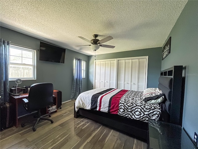 bedroom featuring hardwood / wood-style flooring, multiple closets, a textured ceiling, and ceiling fan