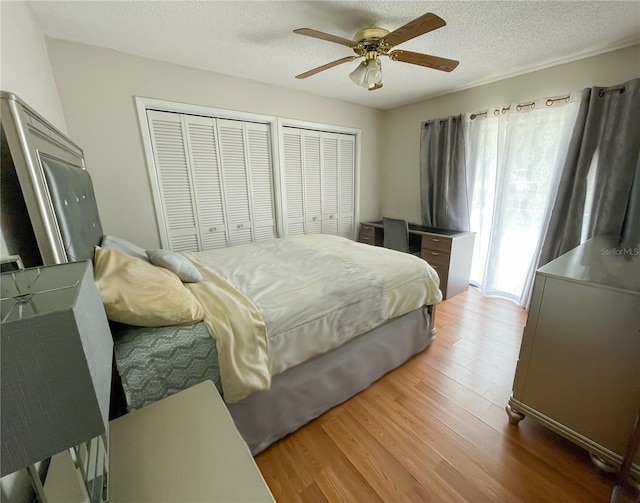 bedroom with ceiling fan, wood-type flooring, a textured ceiling, and two closets