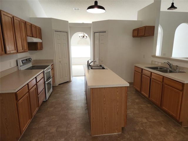 kitchen with range with two ovens, an island with sink, sink, and pendant lighting