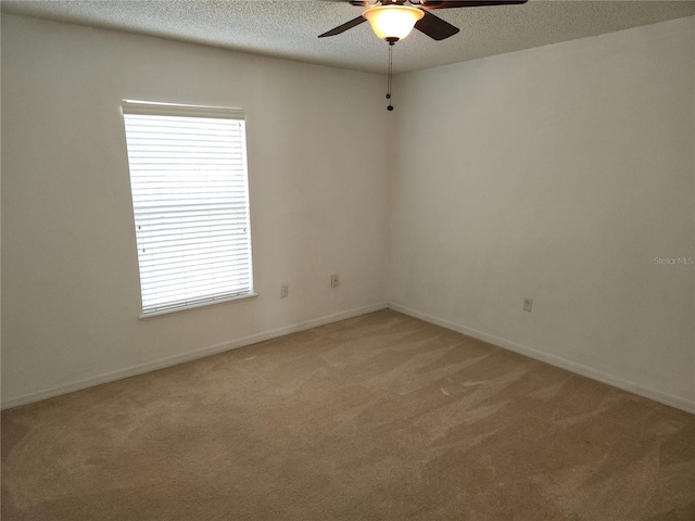 spare room featuring ceiling fan, a wealth of natural light, light colored carpet, and a textured ceiling