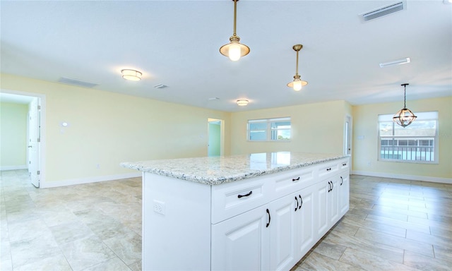 kitchen featuring hanging light fixtures, light tile patterned floors, light stone countertops, a center island, and white cabinetry