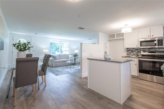 kitchen with tasteful backsplash, white cabinets, light stone counters, light hardwood / wood-style floors, and appliances with stainless steel finishes