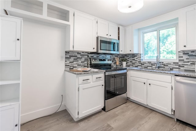 kitchen featuring light stone counters, stainless steel appliances, a sink, white cabinets, and open shelves