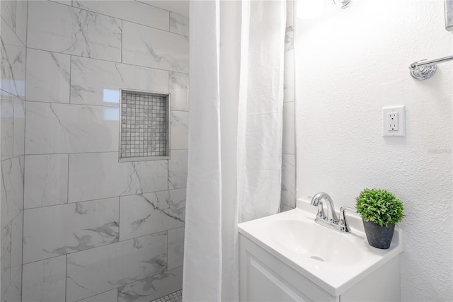 full bathroom featuring tiled shower, a textured wall, and vanity