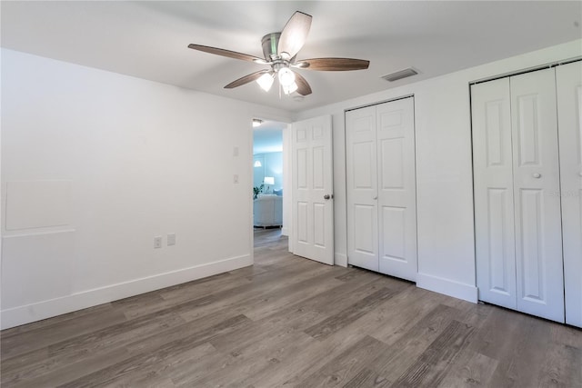 unfurnished bedroom with two closets, visible vents, a ceiling fan, light wood-type flooring, and baseboards