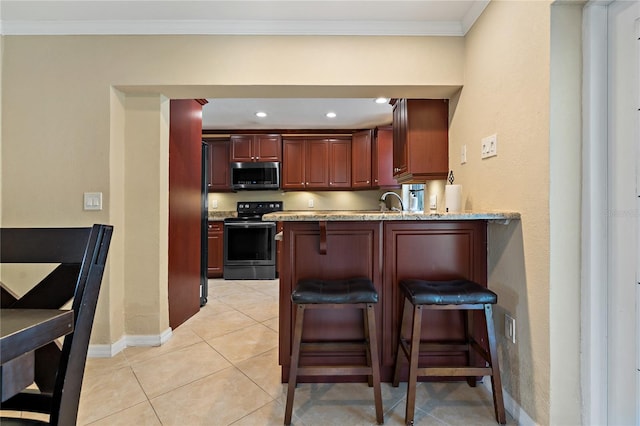 kitchen with light tile patterned floors, kitchen peninsula, light stone counters, electric range oven, and a kitchen bar