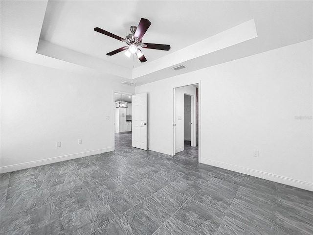 tiled empty room featuring ceiling fan and a raised ceiling