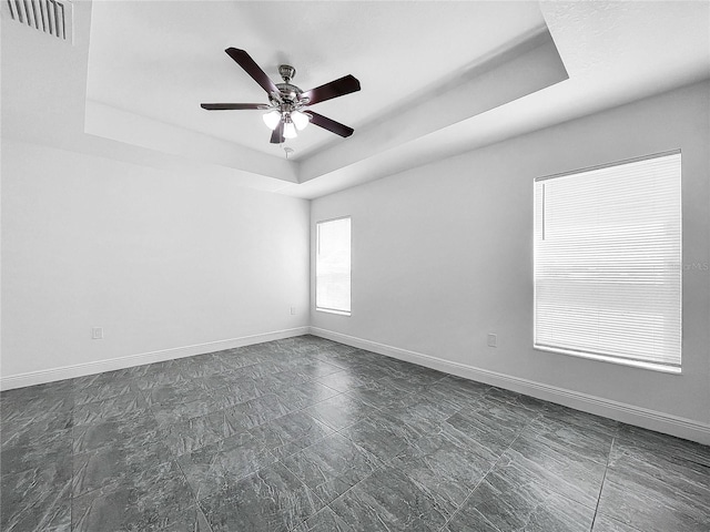 unfurnished room featuring dark tile patterned flooring, ceiling fan, and a raised ceiling