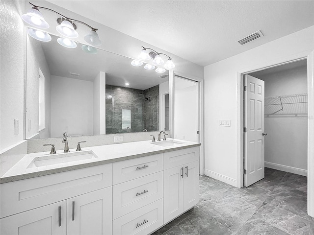 bathroom featuring a tile shower, tile patterned floors, a textured ceiling, and double vanity