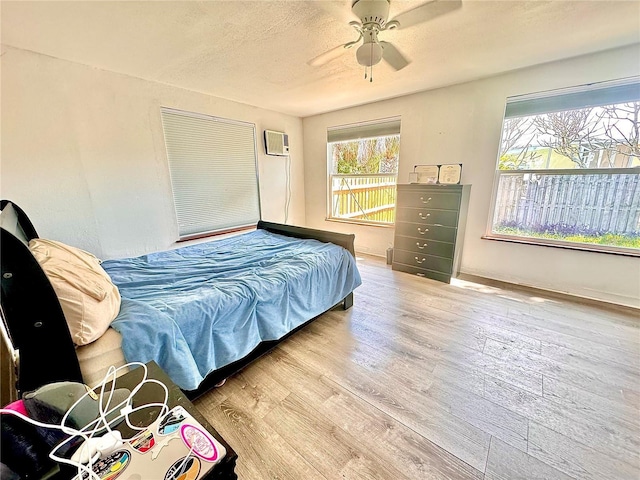 bedroom featuring hardwood / wood-style flooring, ceiling fan, a wall mounted AC, and a textured ceiling