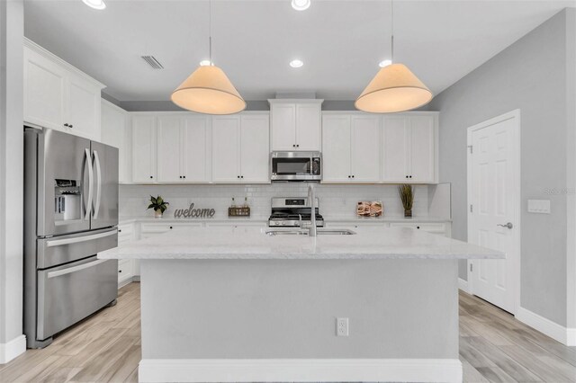 kitchen featuring white cabinetry, tasteful backsplash, an island with sink, light hardwood / wood-style floors, and appliances with stainless steel finishes