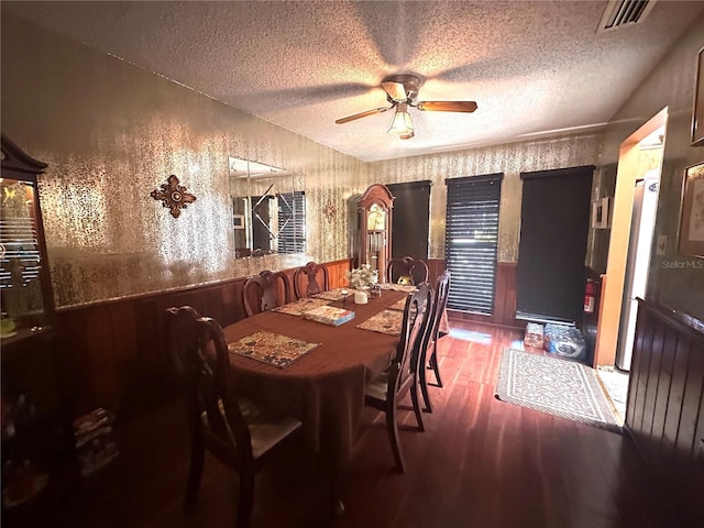 dining space with dark hardwood / wood-style flooring, wooden walls, a textured ceiling, and ceiling fan