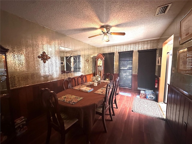 dining room featuring ceiling fan, dark hardwood / wood-style flooring, a textured ceiling, and wood walls