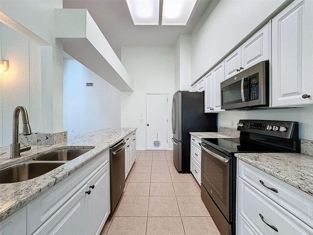 kitchen featuring light stone countertops, appliances with stainless steel finishes, sink, light tile patterned floors, and white cabinetry