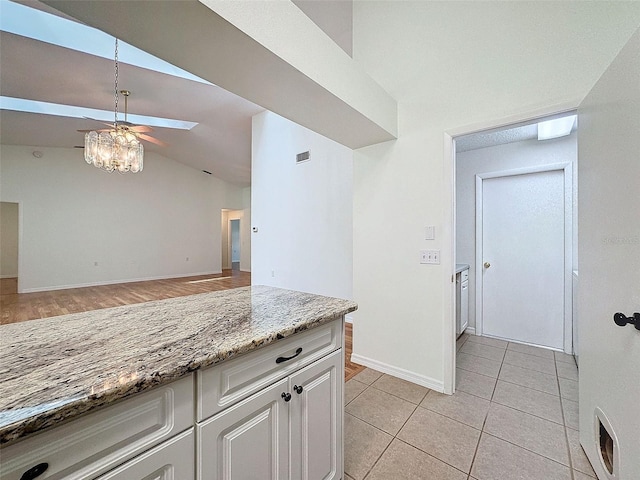 kitchen with light stone counters, vaulted ceiling with skylight, ceiling fan, white cabinets, and light tile patterned flooring