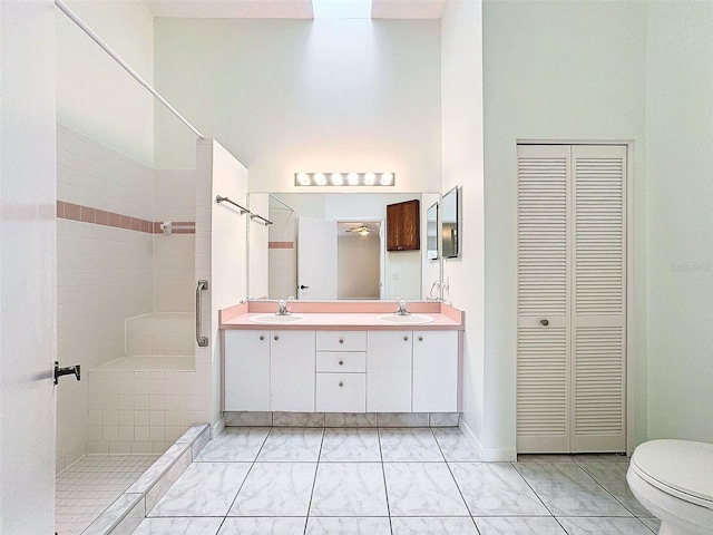 bathroom with vanity, toilet, a towering ceiling, and tiled shower