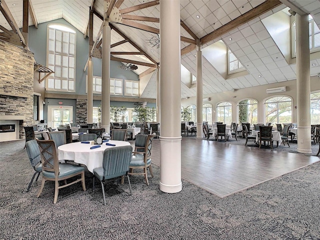 dining space featuring beam ceiling, a stone fireplace, high vaulted ceiling, dark hardwood / wood-style floors, and decorative columns