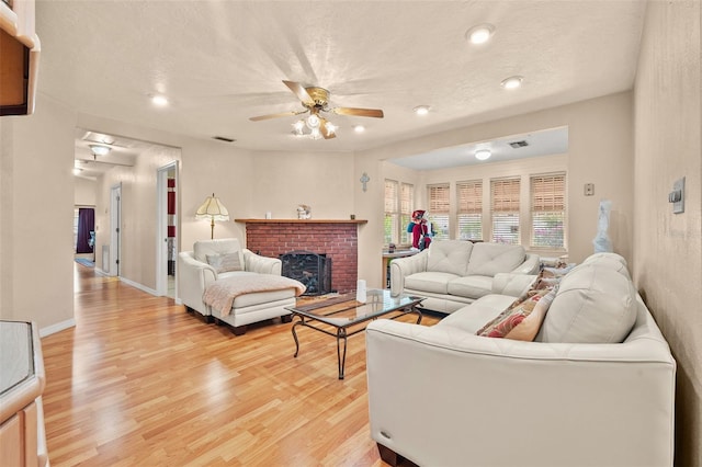 living room featuring ceiling fan, a brick fireplace, a textured ceiling, and light hardwood / wood-style floors