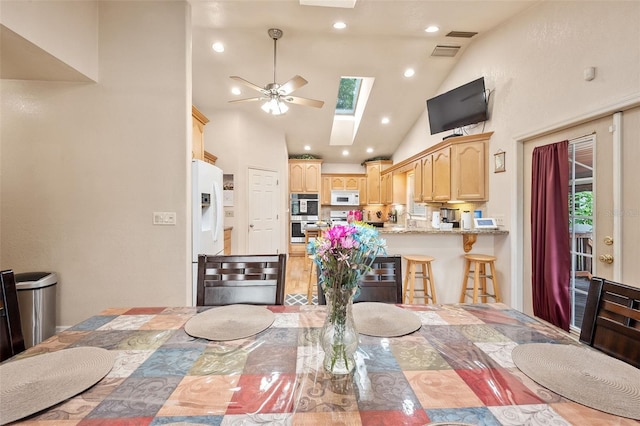 dining space with ceiling fan, a skylight, and high vaulted ceiling