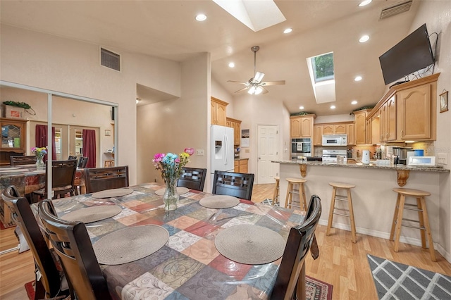 dining room featuring ceiling fan, high vaulted ceiling, light wood-type flooring, and a skylight