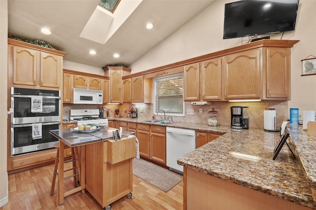 kitchen with sink, white appliances, lofted ceiling with skylight, a kitchen breakfast bar, and light wood-type flooring