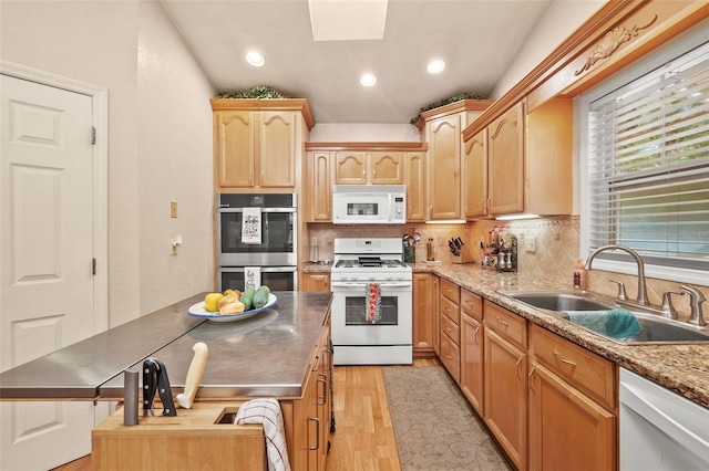 kitchen featuring sink, white appliances, a skylight, decorative backsplash, and light wood-type flooring