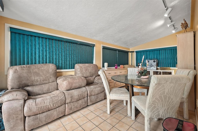 dining space featuring rail lighting, vaulted ceiling, a textured ceiling, and light tile patterned floors