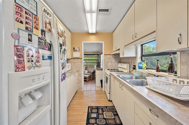 kitchen featuring sink, tasteful backsplash, white appliances, light hardwood / wood-style floors, and cream cabinetry