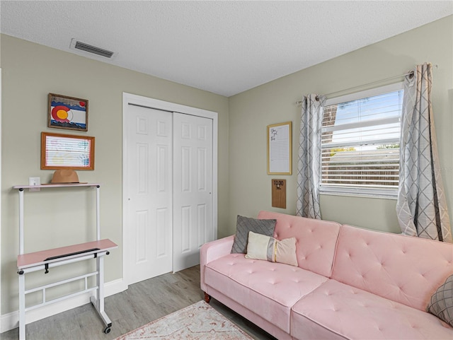 living room featuring baseboards, a textured ceiling, visible vents, and wood finished floors