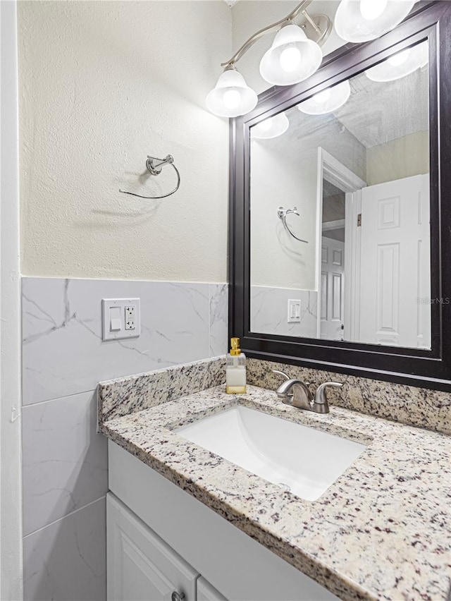 bathroom featuring a textured wall, wainscoting, tile walls, and vanity