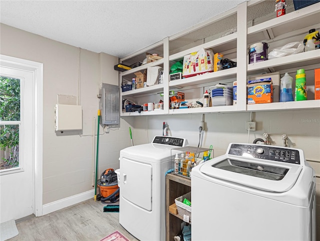 laundry area with washing machine and dryer, a textured ceiling, light hardwood / wood-style floors, and electric panel