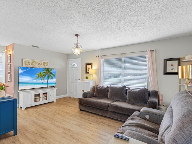 living room with a textured ceiling, visible vents, light wood-style flooring, and baseboards