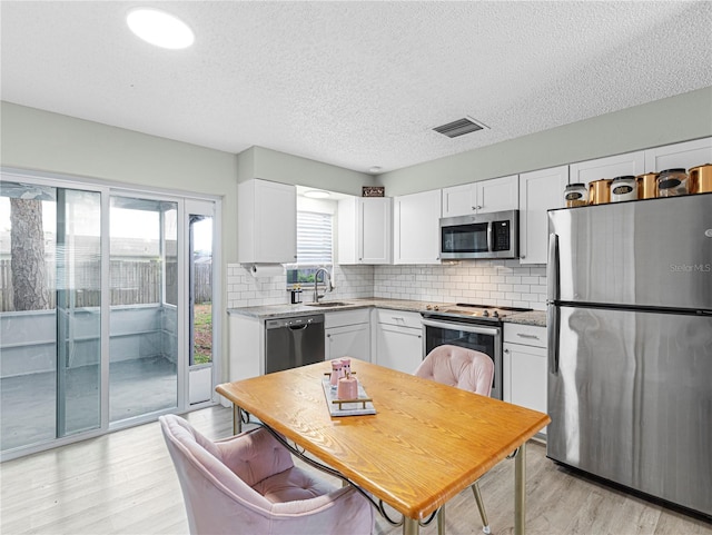 kitchen with visible vents, appliances with stainless steel finishes, a sink, white cabinetry, and backsplash