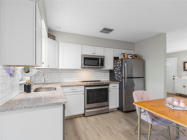 kitchen with white cabinetry, stainless steel appliances, light stone counters, light hardwood / wood-style floors, and backsplash